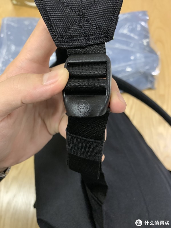 没查到这个扣具，看着应该是Herschel的缩写，塑料材质。有卷背带的收束带