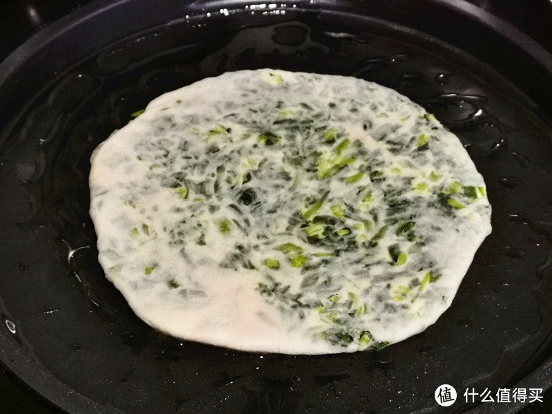 平底锅中倒入剩余的花生油，抹平，将韭菜油饼用擀面杖卷起来放在锅中，开小火烙；