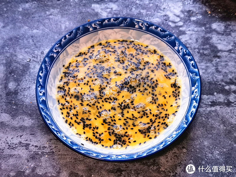 把鸡蛋磕入盘子里，用筷子搅散，尽量搅至白糖融化，黑芝麻分布均匀一些；